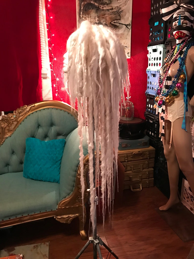 Puede incluir: Peluca de rastas blancas en un tr&iacute;pode. La peluca es larga y fluida, con un fondo blanco.