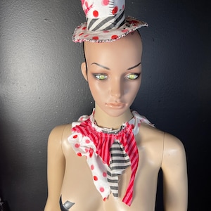 Puede incluir: Un sombrero de copa hecho a mano con un estampado de lunares rojos y blancos, detalles de rayas blancas y negras y un cuello con volantes a juego. El sombrero se asegura con una fina diadema. El cuello presenta tela roja, blanca y negra.
