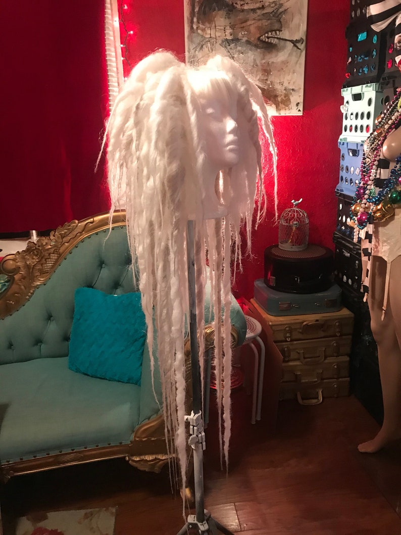 Puede incluir: Peluca de rastas blancas en una cabeza de maniqu&iacute;, la peluca es larga y fluida, el maniqu&iacute; est&aacute; en un soporte con una base de tr&iacute;pode.