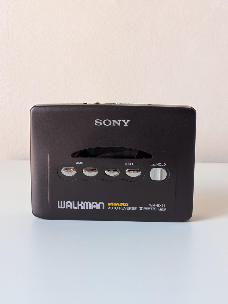 May include: A black Sony Walkman cassette player featuring the model number WM-EX53, Mega Bass, and Auto Reverse technology. The device includes silver control buttons labeled AMS, BATT, and a white sliding HOLD switch on the front panel.