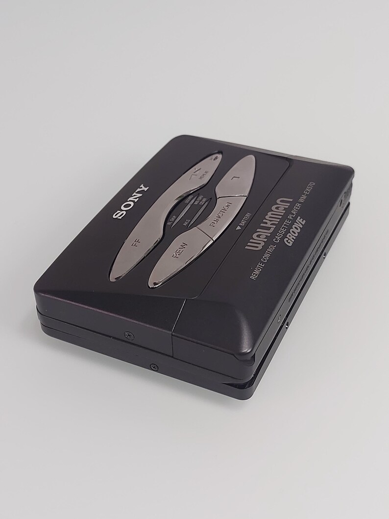 May include: Black Sony Walkman cassette player with silver controls. The device features the word "SONY" on the top left and "WALKMAN" on the bottom right. The model is WM-EX570. It has buttons for rewind, fast forward, and other functions.