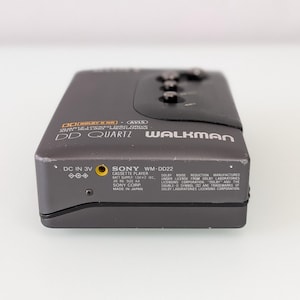 May include: A dark grey Sony WM-DD22 Walkman cassette player. The device has the text "DD Quartz Walkman" and "Dolby B NR" printed on the front. The bottom of the device has the text "Sony WM-DD22" and other technical information.
