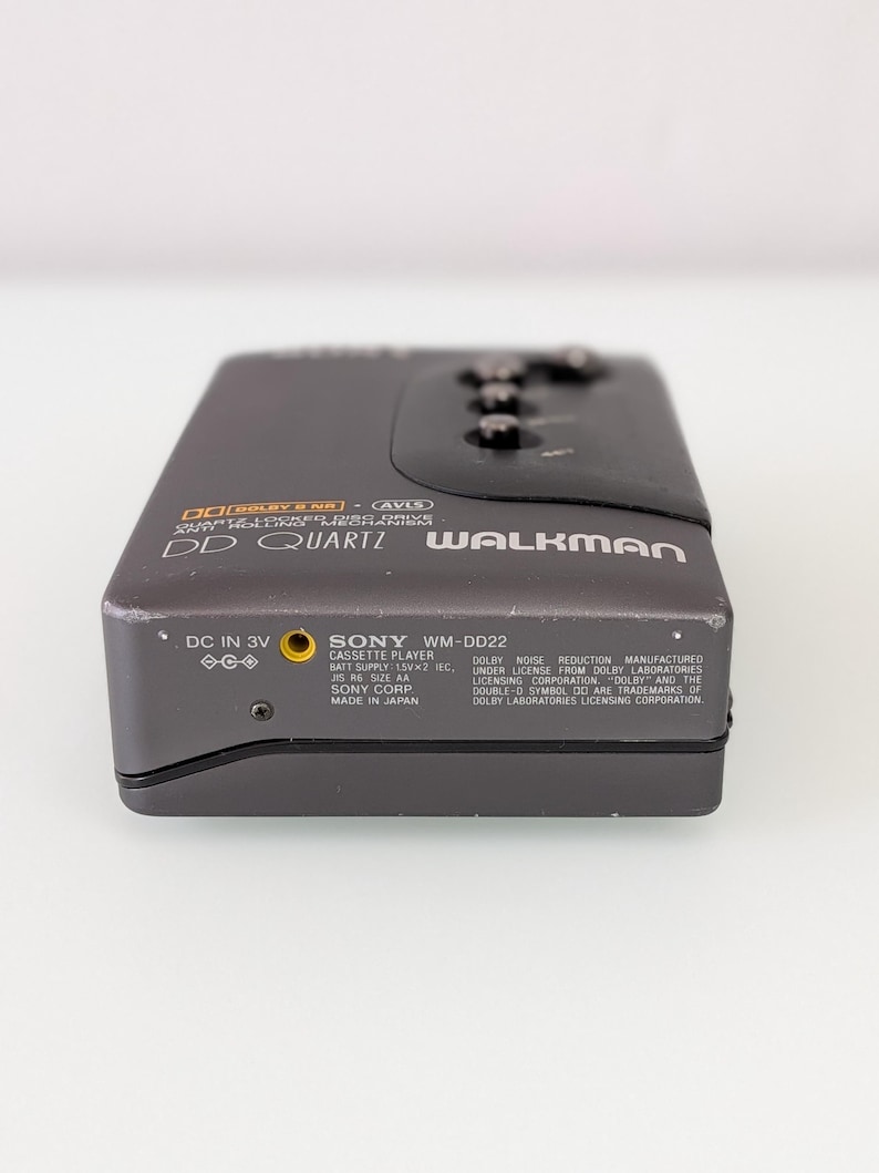 May include: A dark grey Sony WM-DD22 Walkman cassette player. The device has the text "DD Quartz Walkman" and "Dolby B NR" printed on the front. The bottom of the device has the text "Sony WM-DD22" and other technical information.