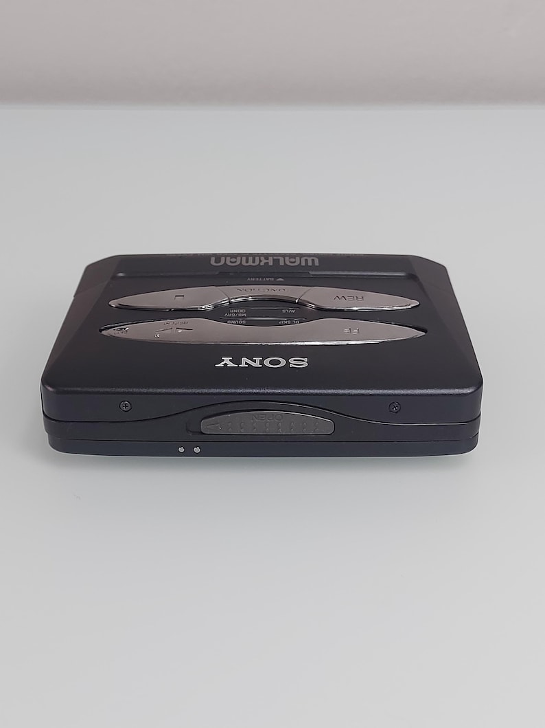 May include: A black Sony Walkman cassette player. The device features silver buttons for rewind, fast forward, and play. The word "WALKMAN" is printed in silver on the top, and "SONY" is printed on the front.