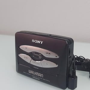 May include: A black Sony Walkman cassette player with silver buttons and the text "WALKMAN" and "GROOVE". The player has a remote control and a battery indicator. The device is a vintage audio player.