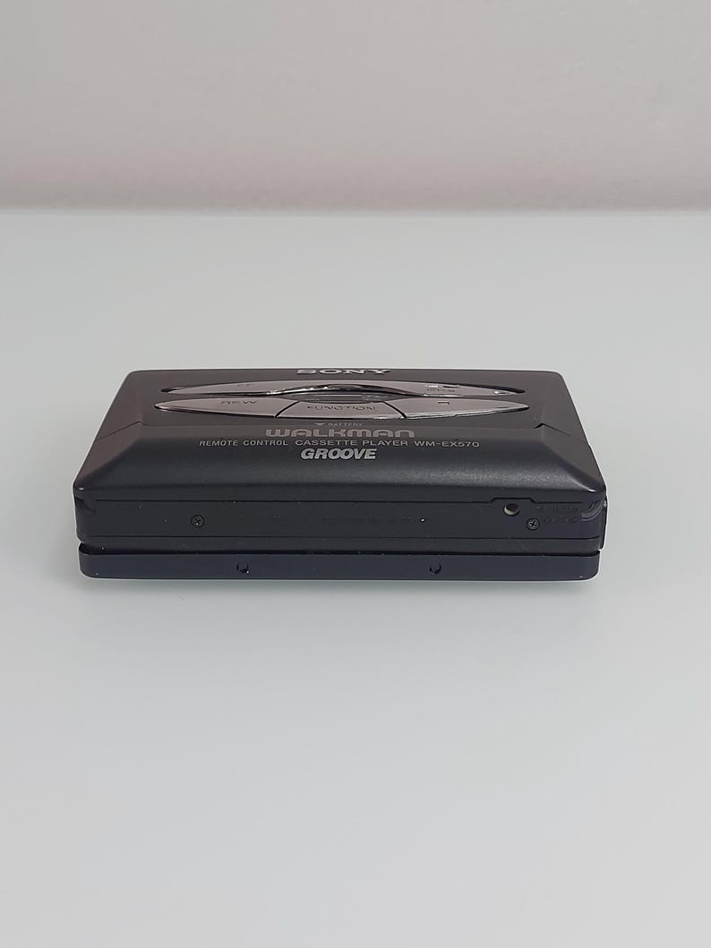 May include: Black Sony Walkman WM-EX570 remote control cassette player. It features silver function buttons and the word "Groove". The device has a rectangular shape and a sleek design.