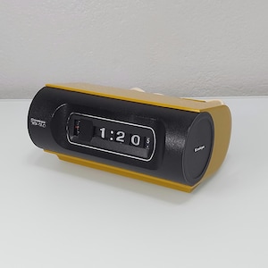 May include: A vintage Sanyo flip clock in black and gold. The clock displays the time as 1:20. The clock has the Sanyo logo on the front and side. The model number is 3G-GLO.