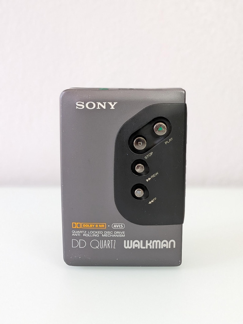 May include: A grey Sony Walkman DD Quartz portable cassette player. The device has a black control panel with play, stop, rewind, and fast forward buttons. The text "SONY" and "WALKMAN" are visible on the device.