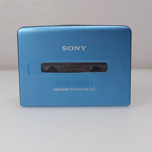 以下が含まれることがあります： 青いソニーウォークマンポータブルカセットプレーヤー。デバイスの上部には「SONY」、前面には「WALKMAN」の文字がプリントされています。プレーヤーには「MEGA BASS」と「AUTO REVERSE」の文字も表示されています。