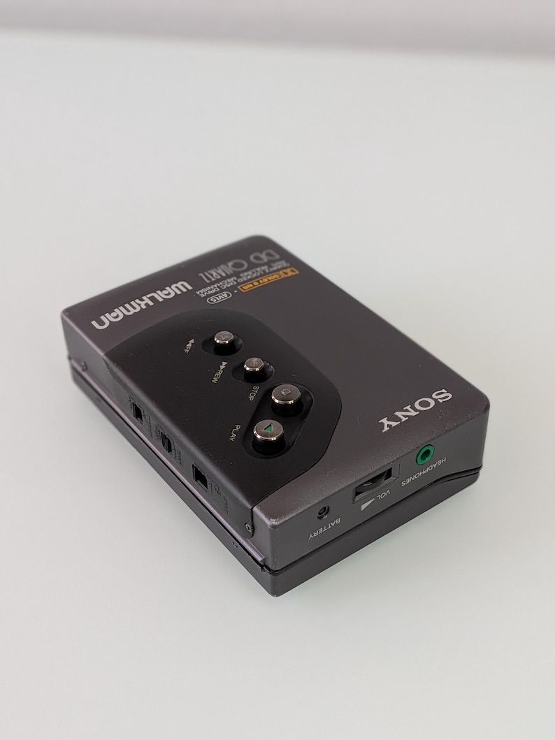 May include: A grey Sony Walkman cassette player with black control buttons. The device has the word "SONY" printed on the side and "WALKMAN" on the top. It features a headphone socket and volume control.