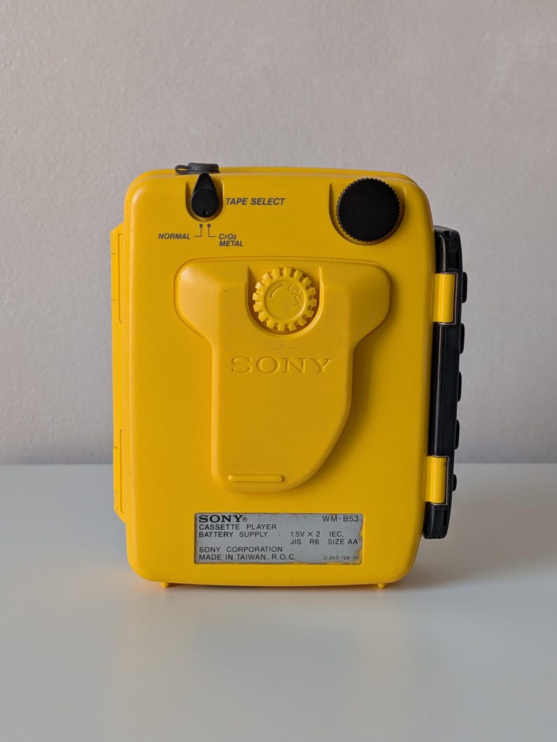 May include: A bright yellow Sony Walkman cassette player, model WM-B53, featuring a central belt clip, a black volume dial, and a tape select switch for Normal, CrO2, and Metal tapes. The device includes a label with technical specifications.