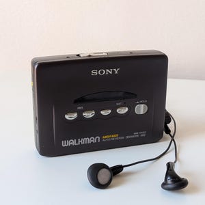 May include: A black Sony Walkman WM-EX53 cassette player with a rectangular body, silver control buttons, and a black wired earphone set. The front features the text SONY, WALKMAN, MEGA BASS, AUTO REVERSE, and WM-EX53 with various function labels.
