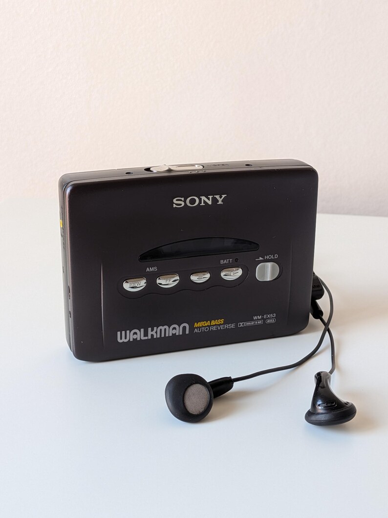 May include: A black Sony Walkman WM-EX53 cassette player with a rectangular body, silver control buttons, and a black wired earphone set. The front features the text SONY, WALKMAN, MEGA BASS, AUTO REVERSE, and WM-EX53 with various function labels.