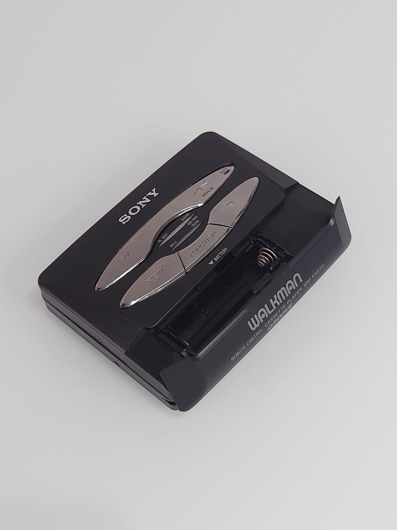 May include: Black Sony Walkman WM-EX570 cassette player with silver control buttons. The portable audio device has a battery compartment and the Walkman logo is visible. The device is on a white background.