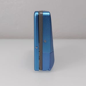 以下が含まれることがあります： 長方形の青い電子機器。デバイスはメタリック仕上げで、中央に濃い灰色のストライプがあります。デバイスは白い表面に直立しています。