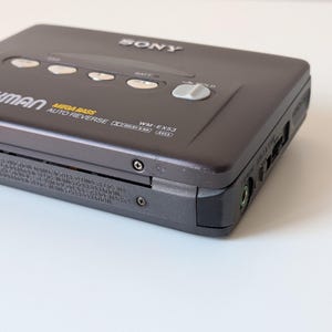 May include: A dark gray Sony Walkman WM-EX53 cassette player featuring Mega Bass, Auto Reverse, and Dolby B NR technology. The device includes silver control buttons, a hold switch, and a headphone jack on the side, with printed model details.