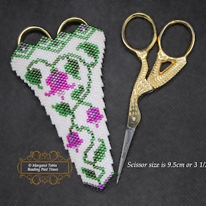 Puede incluir: Estuche para tijeras de cuentas blancas con un diseño floral con cuentas rosas y verdes. El estuche está diseñado para contener un par de pequeñas tijeras doradas, que miden 9,5 cm de largo. El texto "Scissor size is 9.5cm or 3 1/2 inches" es visible debajo de las tijeras.