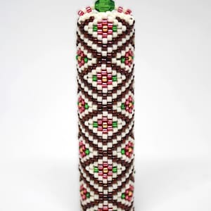 Puede incluir: Un tapón de botella de cuentas con un patrón geométrico marrón, blanco, rosa y verde. El tapón está rematado con un cristal verde.