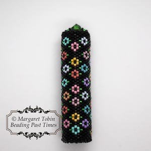 Peut inclure: Un capuchon de stylo noir perlé avec un sommet en cristal vert et un motif floral coloré.
