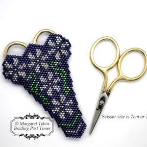 Könnte beinhalten: Ein bestickter Scherenhalter in Marineblau, Weiß und Grün mit einem Blumenmuster. Der Halter ist für eine kleine goldene Schere konzipiert, die 7 cm oder 2 3/4 Zoll lang ist. Der Text "Margaret Tobin Beading Past Times" ist in der linken unteren Ecke des Bildes sichtbar.