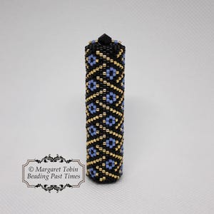 Peut inclure: Un tube perlé noir et or avec un motif géométrique bleu et or. Le tube est surmonté d'une perle noire.