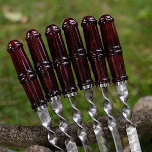 May include: Set of six silver skewers with dark wood handles. The skewers have a twisted design and a diamond-shaped pattern on the metal.