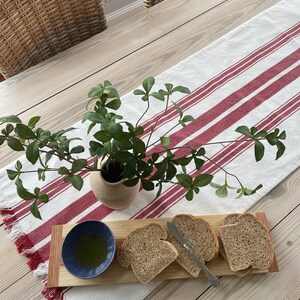 May include: A wooden serving board with four slices of bread and a small blue bowl with olive oil. The board is on a white and red striped table runner.