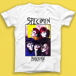 May include: White t-shirt with a colorful graphic of the band Specimen. The graphic features five band members with the band's name "Specimen" and the album title "Catastrophe" printed in black.