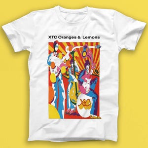 Puede incluir: Camiseta blanca con un gráfico colorido de una banda tocando música. El gráfico presenta un esquema de color rojo, amarillo y azul con el texto "XTC Oranges & Lemons".