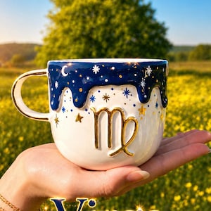 May include: A white ceramic mug with a gold handle and the Virgo zodiac symbol in gold. The top of the mug is navy blue with white stars and gold accents. The word "Virgo" is displayed in gold text.