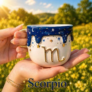 May include: A white ceramic mug featuring a dark blue drip design at the rim with gold star accents. The mug displays a raised gold Scorpio zodiac symbol on the front. The word Scorpio is printed in blue text below the mug, decorated with gold stars.