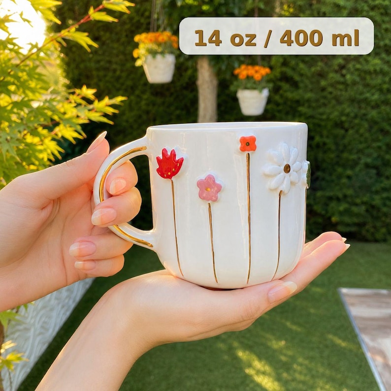May include: White ceramic mug with a gold handle and floral embellishments. The mug features red, pink, and white flowers with gold stems. The mug holds 14 oz / 400 ml of liquid.