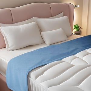 Könnte beinhalten: Ein Bett mit rosa Kopfteil, weißen Kissen und einer blauen Decke. Die weiße Matratze hat ein gestepptes Design. Eine kleine Topfpflanze steht auf dem Nachttisch.