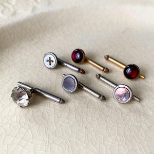May include: Six cufflinks with different coloured stones and designs. The cufflinks are silver and gold toned. The stones are red, clear, and iridescent.