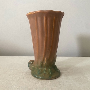 May include: A brown ceramic vase with a green glaze and a unique, sculpted base. The vase has a flared opening and a textured, ribbed surface.