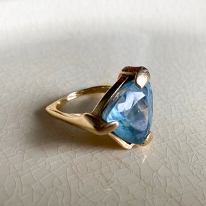 May include: A gold ring with a large, triangular, light blue gemstone.