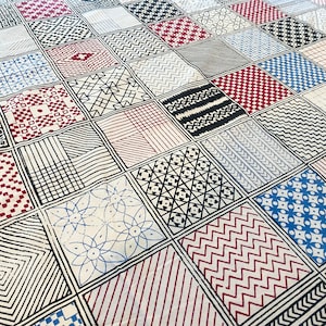 May include: A white fabric with a patchwork design featuring various black and white geometric patterns, including squares, diamonds, and stripes. Some of the squares have red and blue accents.