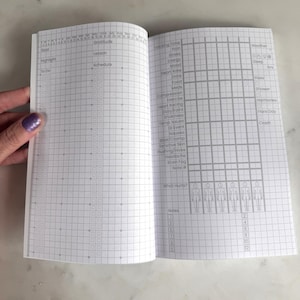 May include: An open planner with white pages and a gray grid layout. The left page features sections for Goal, Highlight, To Do, Gratitude, Lesson, and Schedule. The right page includes tracking columns for health metrics, daily habits, and body diagrams.