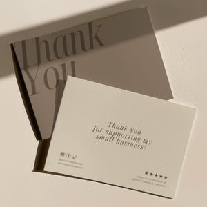 May include: Two rectangular cards with a cream-colored finish. The top card features the text Thank You in large dark lettering. The bottom card displays the text Thank you for supporting my small business, social media icons, a website placeholder, and five stars with the text LOVED YOUR PRODUCT OR SERVICE? LEAVE US A REVIEW!