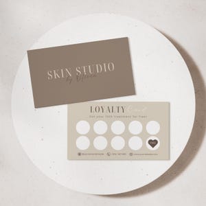 Op de afbeelding: Twee visitekaartjes op een wit oppervlak. De bovenste kaart is taupe met "SKIN STUDIO by Olivia" in een lichtbruin lettertype. De onderste kaart is beige met "LOYALTY Card" en een reeks cirkels.