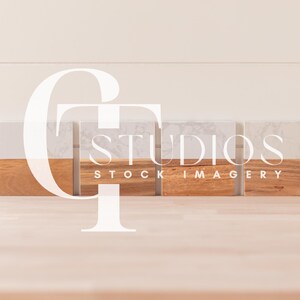 May include: Four white marble coasters with a wood base. The coasters are arranged in a row on a light wood surface. The text "GT Studios Stock Imagery" is printed on the coasters.