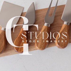 Puede incluir: Cuatro cuchillos para queso con mangos de madera sobre una tabla de cortar de madera. Los cuchillos tienen hojas plateadas y están dispuestos en fila.