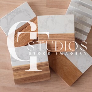 May include: Four square wooden coasters with a white marble top. The coasters have a natural wood finish and are arranged on a light wood surface.