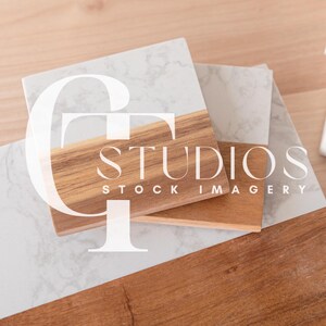 May include: Two white marble coasters with a wooden base. The coasters are stacked on top of each other. The wooden base has the text "STUDIOS STOCK IMAGERY" printed on it.