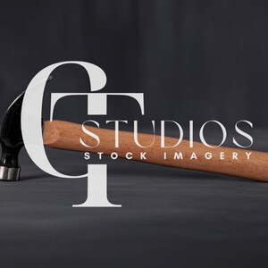 Puede incluir: Un martillo negro con mango de madera yace sobre una superficie gris oscuro. El martillo está parcialmente oscurecido por el texto blanco "GT STUDIOS STOCK IMAGERY".