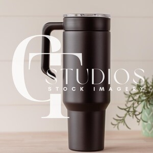 May include: A black stainless steel tumbler with a lid and a handle. The tumbler is on a light brown surface.