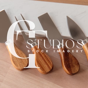 May include: Set of four cheese knives with wooden handles. The knives have different blade shapes and are arranged on a white marble cutting board.