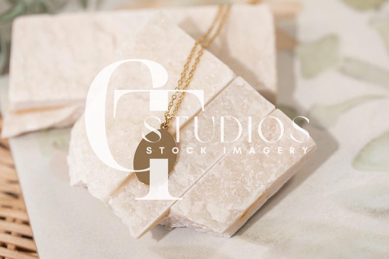 Puede incluir: Un collar dorado con un colgante ovalado descansa sobre una pila de bloques rectangulares de color claro. Los bloques est&aacute;n dispuestos sobre una superficie con un dise&ntilde;o sutil. La imagen tiene el texto "STUDIOS STOCK IMAGERY".