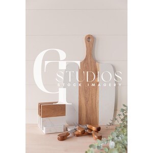 Puede incluir: Una tabla de cortar de madera con un borde pintado de blanco, un juego de posavasos de madera y un juego de pequeños cuchillos con mango de madera sobre una superficie de madera clara.