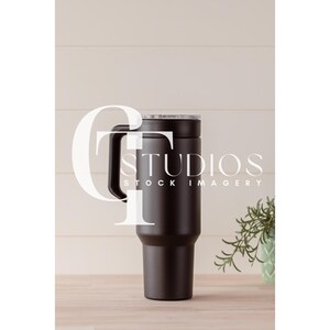 Puede incluir: Una taza de viaje de acero inoxidable negro con tapa y asa. La taza está sobre una superficie de madera marrón claro.